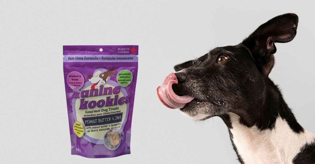 Excited dog with tongue out next to Kanine Kookies Peanut Butter & Jam dog treats package